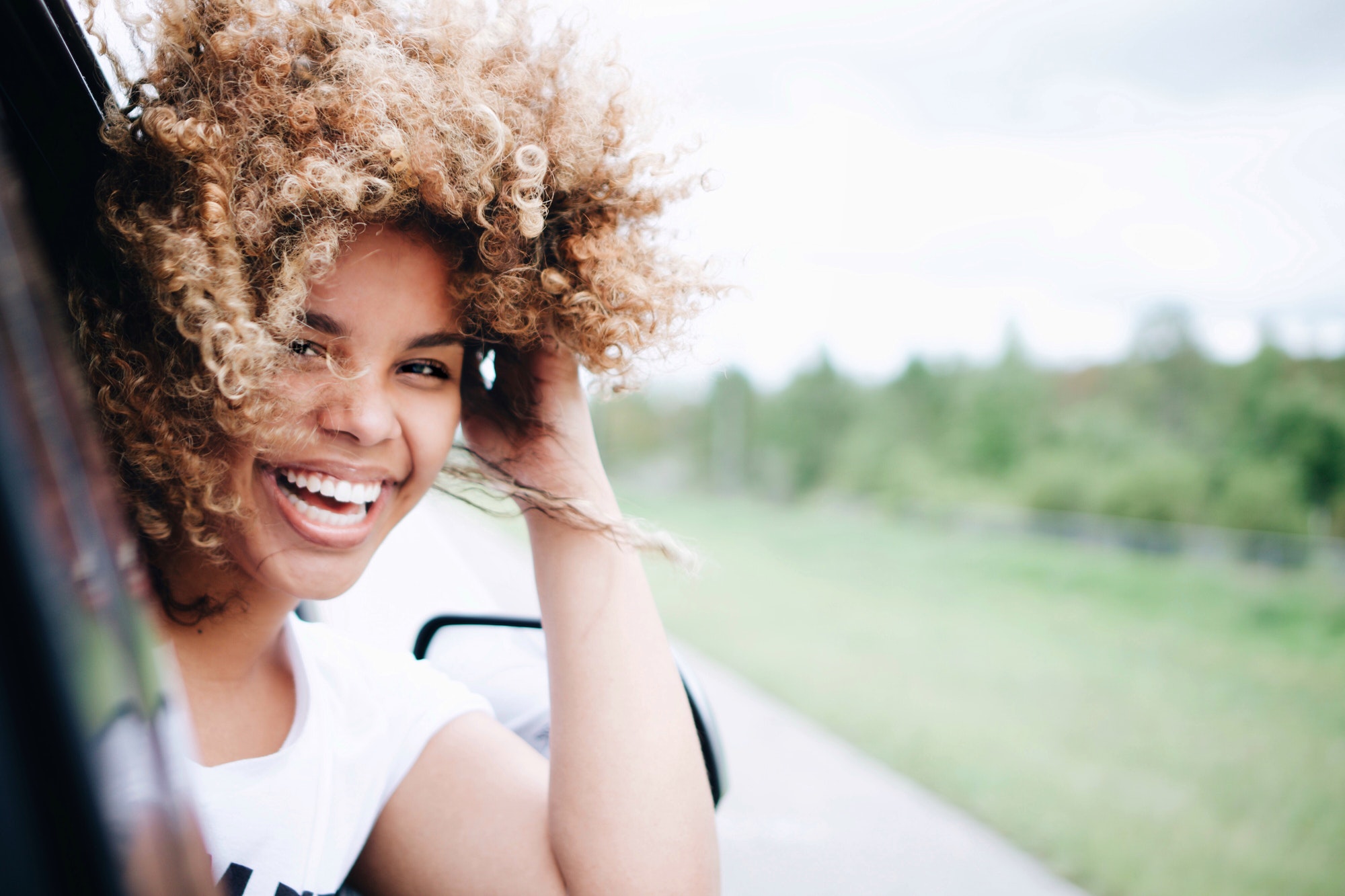 Happy debt free woman smiling with curly hair blowing in the wind on a road trip feeling free